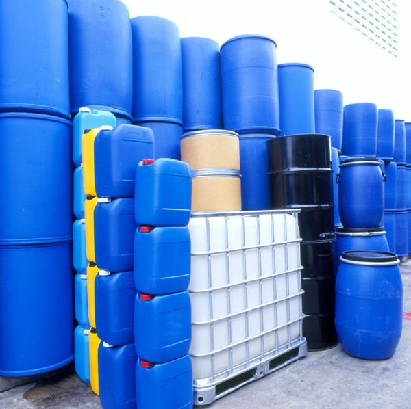 Blue plastic drums, jerrycans and an IBC tote arranged in a bulk chemical yard